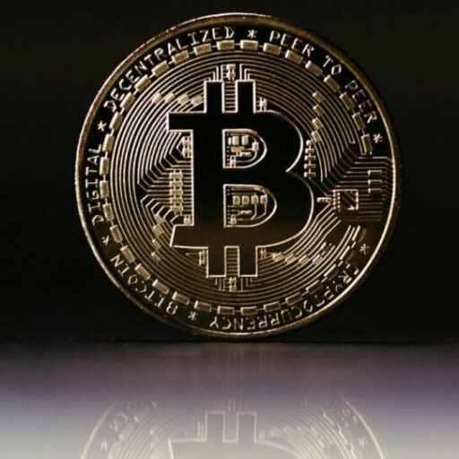 Close-up of a shiny gold Bitcoin coin reflecting against a dark background, symbolizing cryptocurrency value.