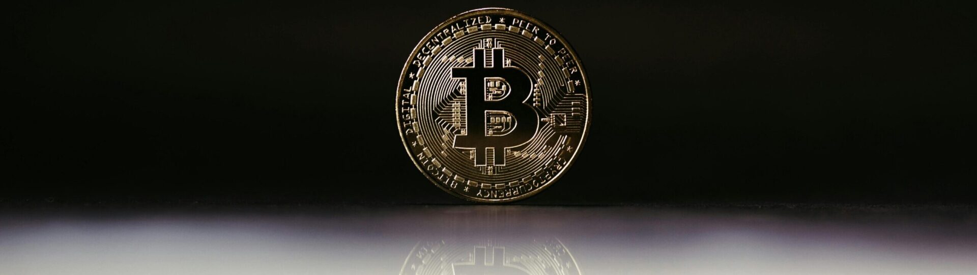 Close-up of a shiny gold Bitcoin coin reflecting against a dark background, symbolizing cryptocurrency value.